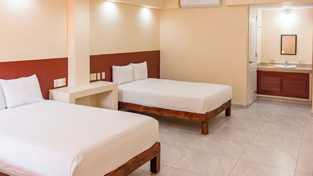 Een hotelkamer met twee bedden, een klein bureau, een badkamer met een wastafel en spiegel, en een airconditioner aan de muur.