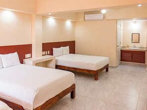 Een hotelkamer met twee bedden, een klein bureau, een badkamer met een wastafel en spiegel, en een airconditioner aan de muur.