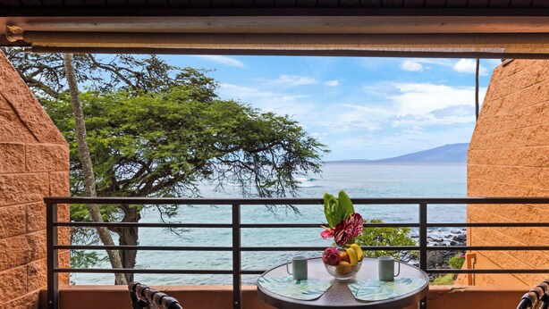 A balcony with a table, chairs, and a view of the sea and mountains. - Kuleana Club #721 Oceanfront-1 bd & 1 ba-3rd Floor (Lahaina)