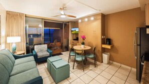A compact living space with a sofa, ottoman, dining table, chairs, a TV, a coffee machine, and a refrigerator. - Kuleana Club #619 Oceanfront - 1 bd & 1 ba- Gated (Lahaina)