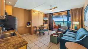 Une chambre d’hôtel moderne dotée d’une kitchenette, d’un coin repas et d’un balcon offrant une vue sur l’océan.