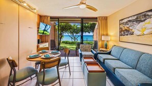 A modern hotel room with a dining area, a sofa, a ceiling fan, and a view of the sea.