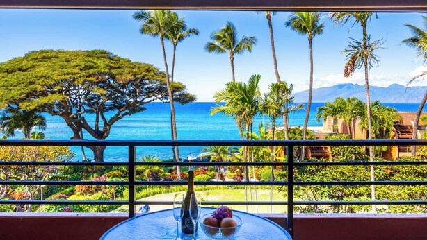 Un balcón con vistas al océano, palmeras y un gran árbol.
