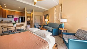 Ein Hotelzimmer mit Bett, einer Couch, einem Esstisch mit Stühlen, einer Küchenzeile und einem Deckenventilator.