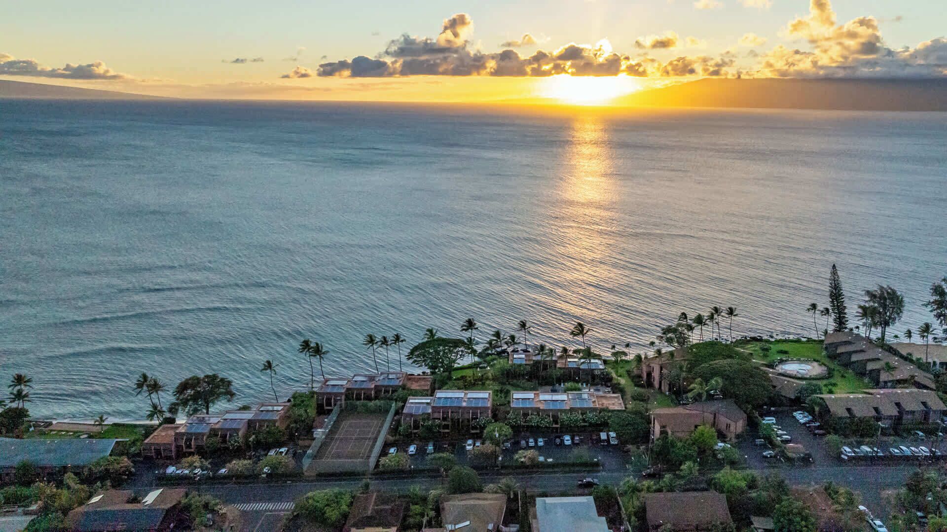 A coastal resort with multiple buildings, a parking area, and a view of the ocean at sunset.