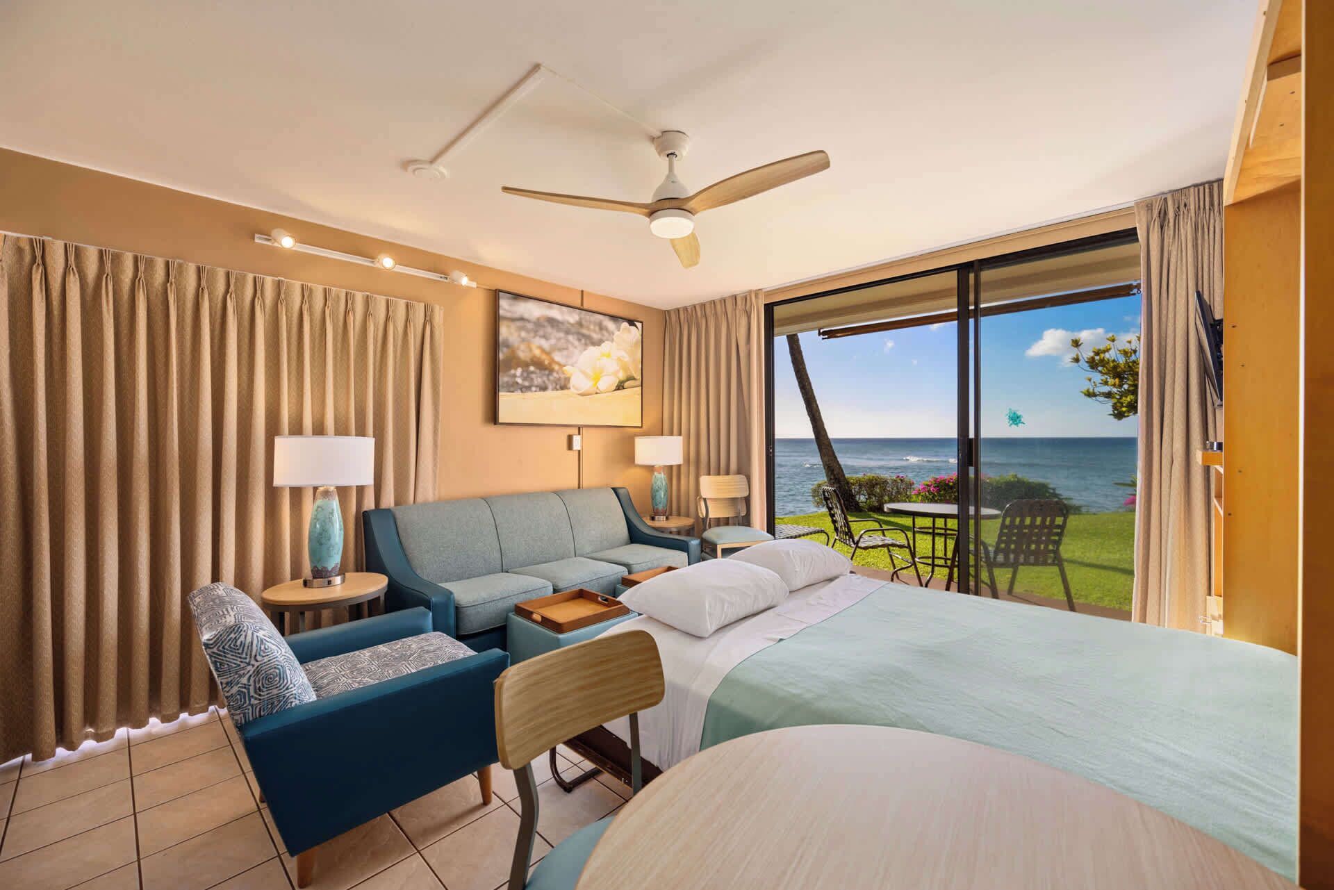 Een hotelkamer met een bed, een bank, een bureau en uitzicht op de oceaan.