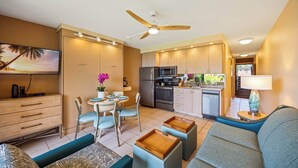 Una cocina moderna con refrigerador, microondas y estufa. Hay un comedor con mesa y sillas, y un área de estar con sofá y otomanas.