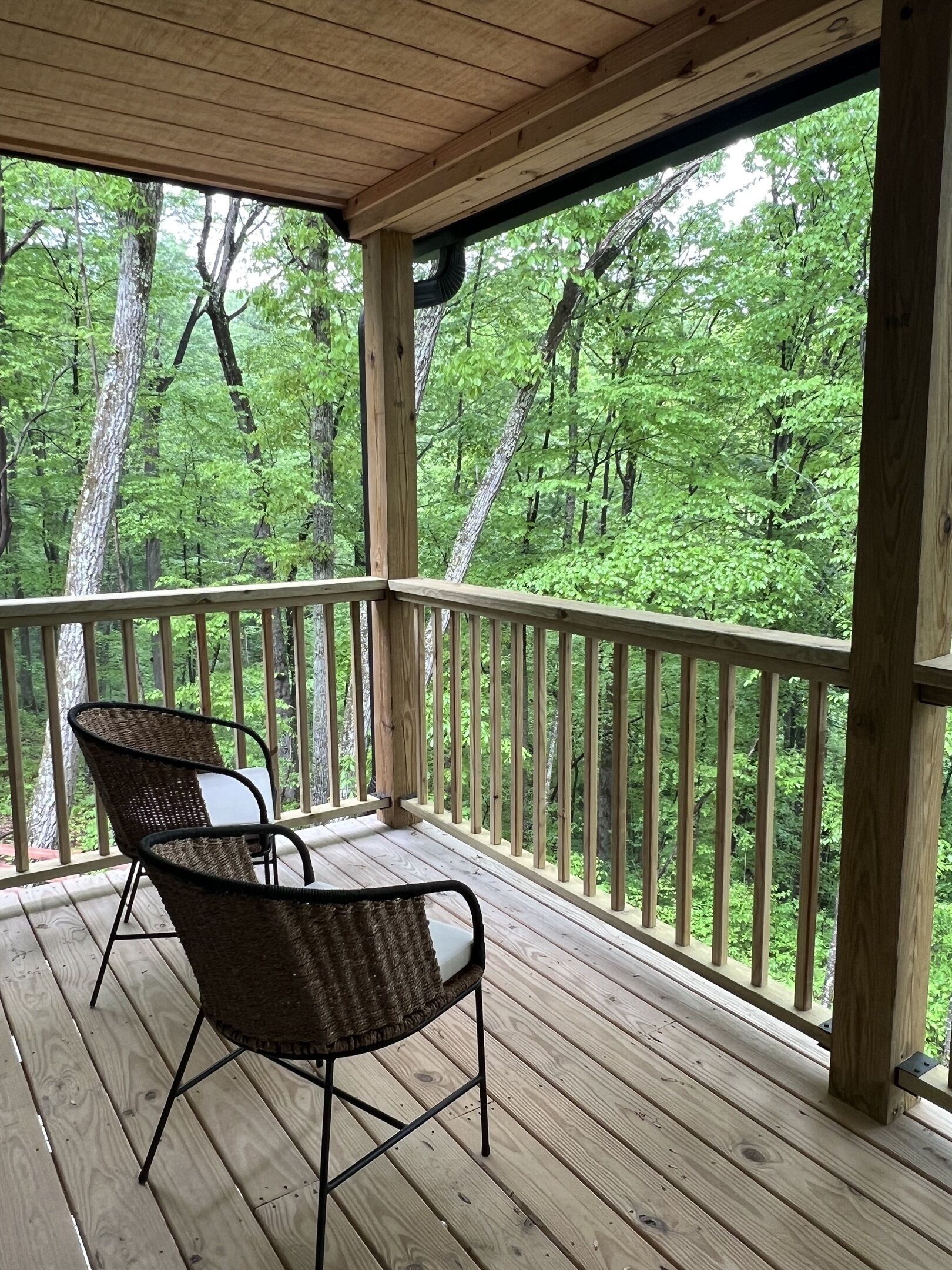 Eine Holzterrasse mit zwei Korbstühlen, mit Blick auf ein bewaldetes Gebiet.