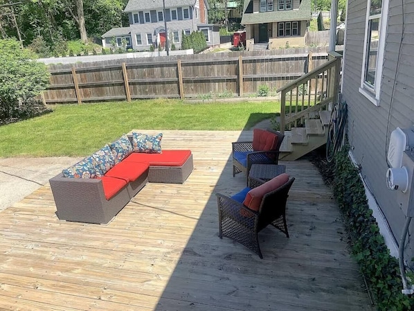 A wooden deck with outdoor furniture, including a sofa and chairs, and a wooden fence in the background.