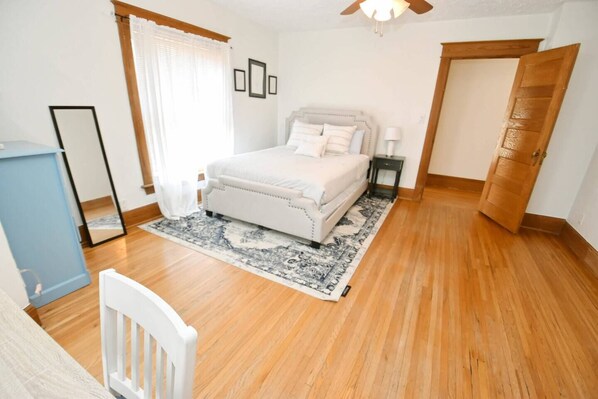 Quarto com cama, mesa de cabeceira e chão de madeira.
