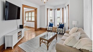 A living room with a flat-screen TV, a sofa, a coffee table, and a television stand. - Historic/Renovated home steps to Notre Dame(103) (South Bend)