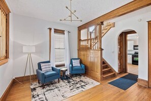 A living room with a staircase, two blue armchairs, a floor lamp, and a rug. - Historic/Renovated home steps to Notre Dame(103) (South Bend)