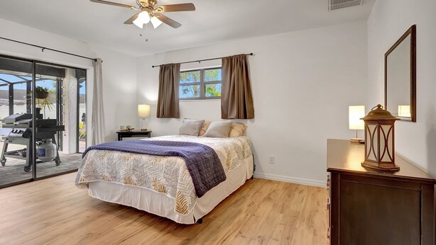 Une chambre à coucher comprenant un lit, un ventilateur de plafond, une fenêtre avec des rideaux, une table de chevet et une lampe.