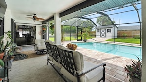 A covered patio area with a pool, seating, and a view of the backyard. - Sunny Pool Retreat, Pet-Friendly Near Beaches (Naples)