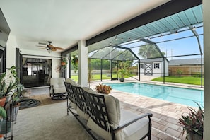 Ein überdachter Patio-Bereich mit Pool, Sitzgelegenheiten und Blick auf den Garten.