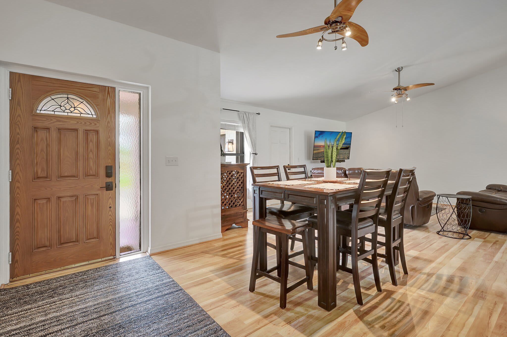 A dining area with a wooden table and chairs, a ceiling fan, and a television on the wall.