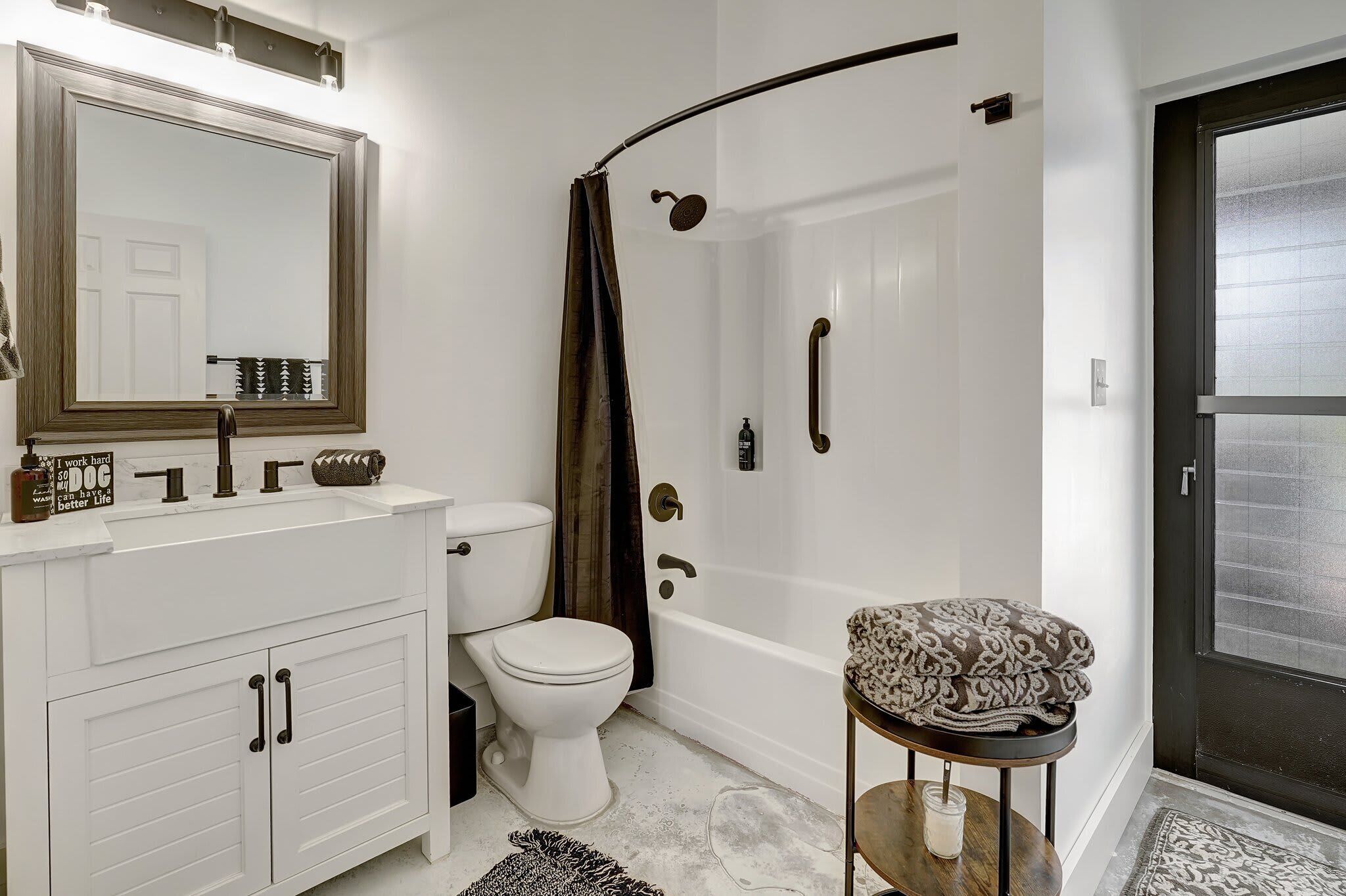 Un baño moderno con un tocador blanco, inodoro, ducha con puerta curva y puerta de cristal que da al exterior.
