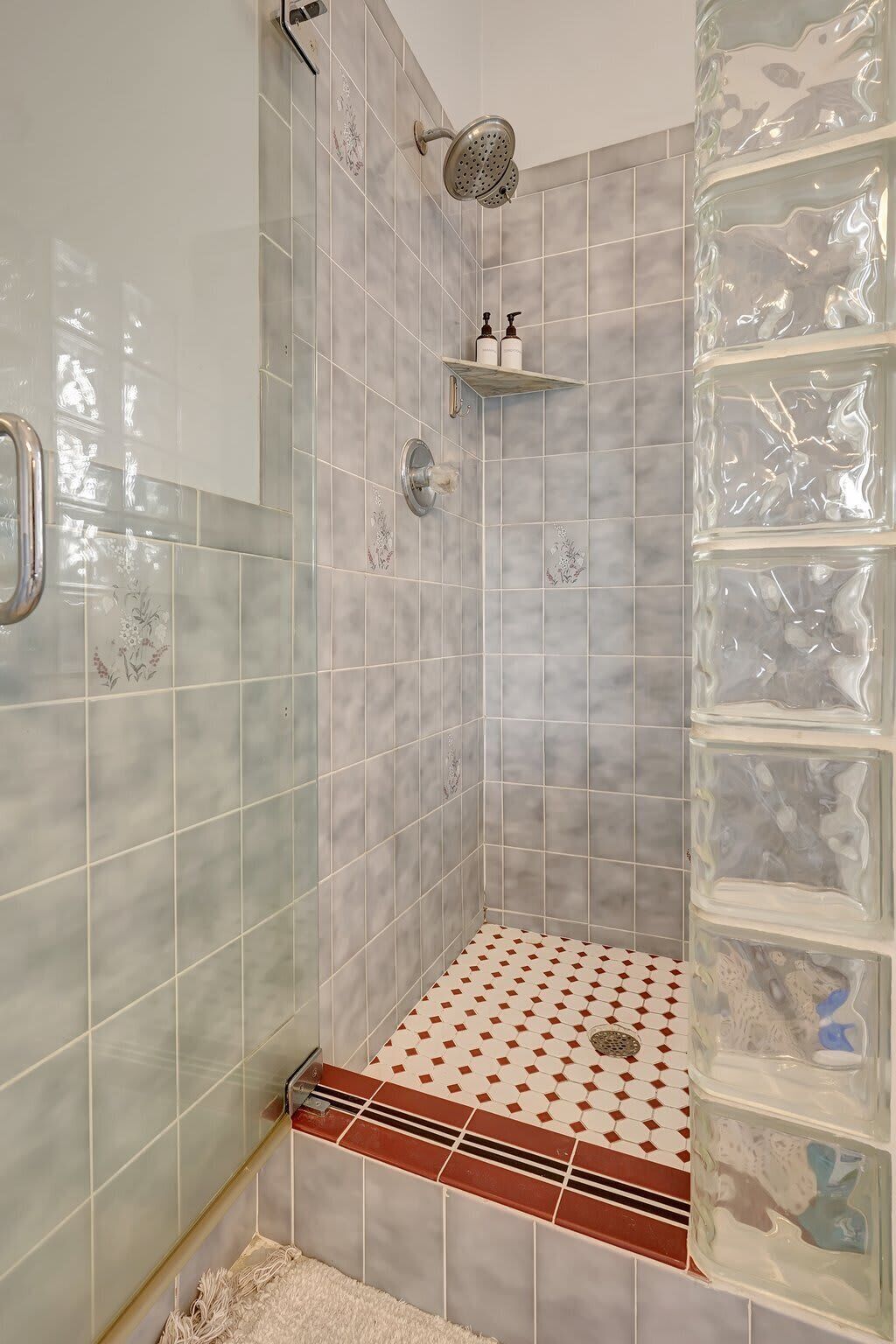 A shower area with a glass shower enclosure, a handheld showerhead, and a shelf with toiletries.