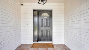 A white brick wall, a dark wooden door with a glass panel, and a welcome mat. - Sunny Pool Retreat, Pet-Friendly Near Beaches (Naples)