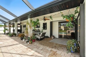 A covered patio area with potted plants, a ceiling fan, and string lights.