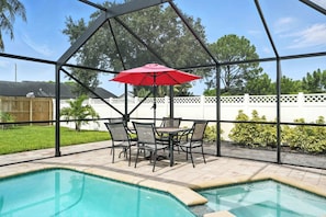 Un espace extérieur abrité comprenant une piscine, du mobilier de jardin et un parasol rouge.