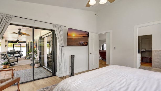 A bedroom with a large bed, a sliding glass door leading to a patio area, and a television mounted on the wall. - Sunny Pool Retreat, Pet-Friendly Near Beaches (Naples)