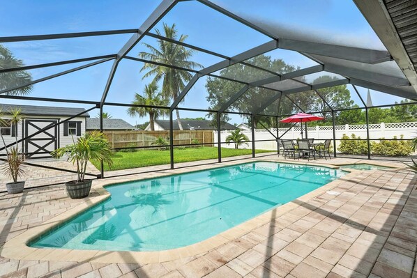 A covered swimming pool with a view of a residential area, including a house and palm trees.