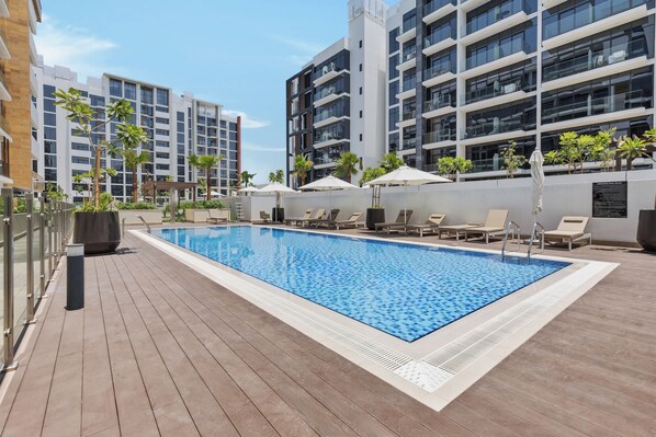 A rooftop pool with lounge chairs and umbrellas, surrounded by modern buildings. - Waves - Azizi Riviera Building 25 Cozy Studio With Balcony (Dubai)