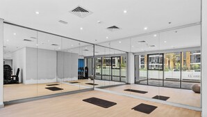 Une salle de sport moderne avec des murs recouverts de miroirs, un plancher en bois et des tapis de sol pour les exercices.