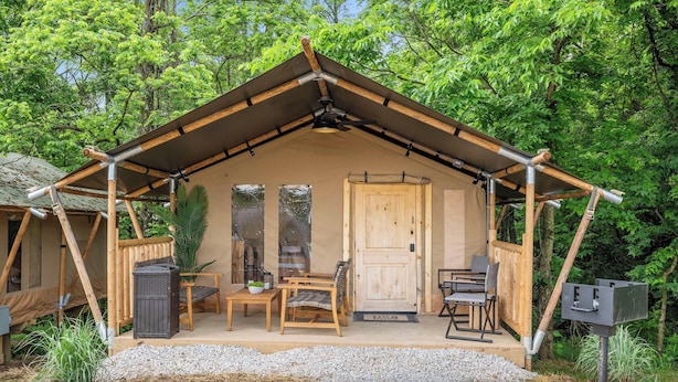 A wooden cabin with a pitched roof, a door, and a porch with two chairs and a table.