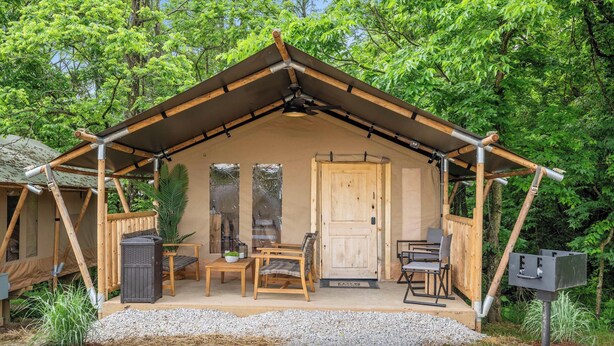 A wooden cabin with a pitched roof, a door, and a porch with two chairs and a table. - Safari Tent D at Eden Reserve - Near Ark (Williamstown)