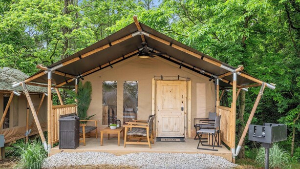 A wooden cabin with a pitched roof, a door, and a porch with two chairs and a table.