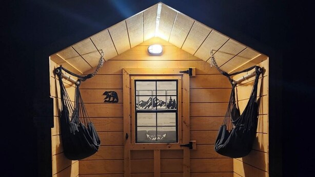A wooden cabin with a sloped roof, a central door, and two hanging hammocks. - Property of Big Foot Roscoe, NY (Roscoe)