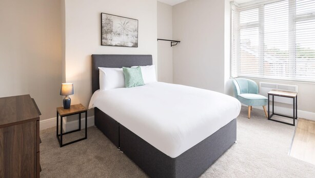 A modern hotel room with a large bed, a nightstand, a chair, and a window with blinds. - Host & Stay | Clifton Studio 2 (Darlington)