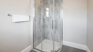 A corner shower with a glass door, a white towel on a metal towel rack, and a grey floor. - Host & Stay | Clifton Studio 2 (Darlington)