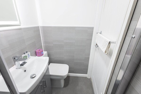 Une petite salle de bain moderne avec un lavabo, des toilettes et une douche, le tout de couleur blanche.