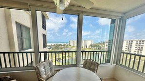 A balcony with a round table and four chairs, overlooking a resort area with buildings and a pool. - Gulf and Bay Club B604 (Siesta Key)