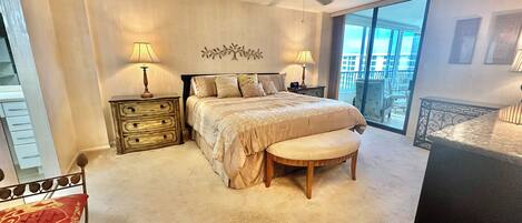 A bedroom with a bed, bedside tables, a bench, a ceiling fan, and a large window with a view.