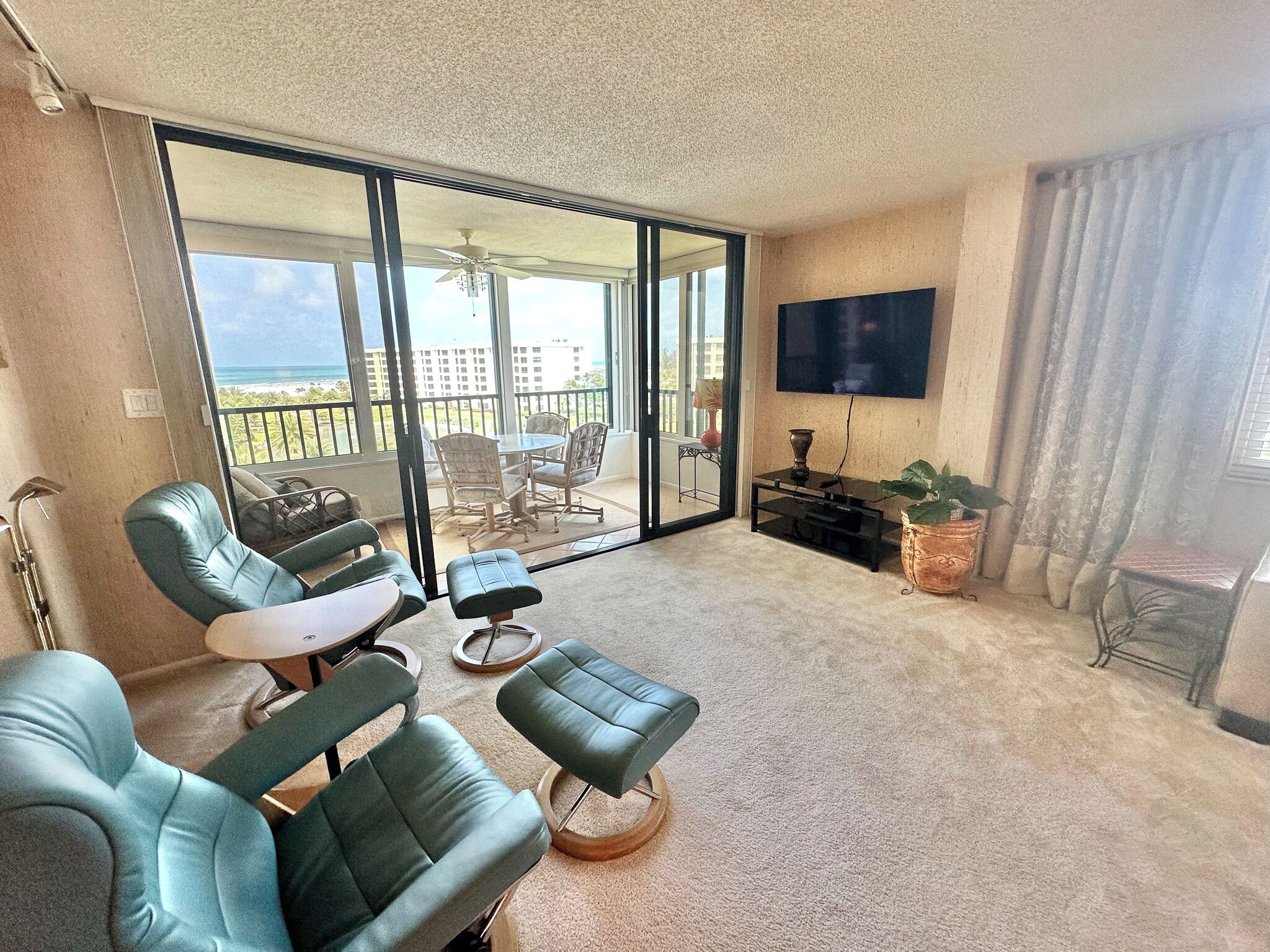 A balcony with a view of the ocean, a seating area with chairs and a table, and a flat-screen TV mounted on the wall.