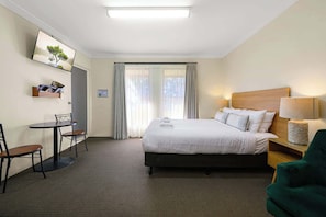 Una habitación de hotel con cama, un escritorio con sillas, un televisor en la pared y una ventana con cortinas.