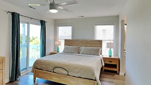 Ein Schlafzimmer mit einem Holzbett, zwei Nachttischen, einem Deckenventilator und Blick durch eine Schiebetür.