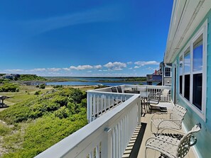 A balcony with outdoor furniture, a view of the sea, and a building with a blue exterior. - Sunset Retreat | Breathtaking Ocean Views, Across from the Beach + Fire Pit! (North Topsail Beach)