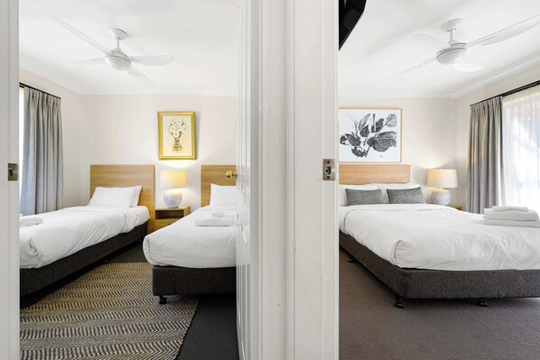 A hotel room with two beds, a ceiling fan, a framed floral artwork, and a patterned rug.