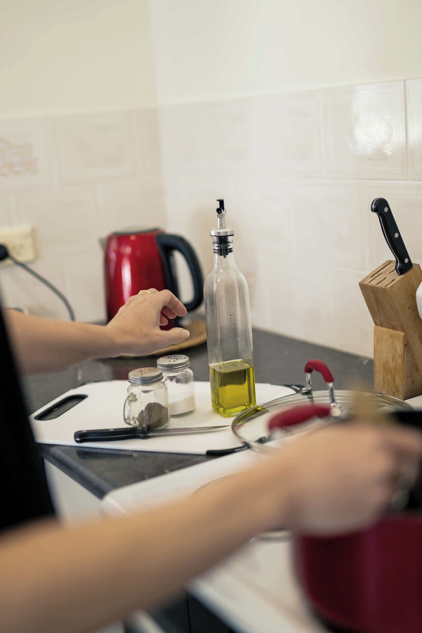 Una encimera de cocina con una tetera, una botella de aceite, saleros y pimenteros, un bloque de cuchillos y una taza roja.