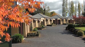 A row of single-story buildings with a gravel driveway leading to the entrance. - Melview Greens - Two-Bedroom Apartment (Orange)