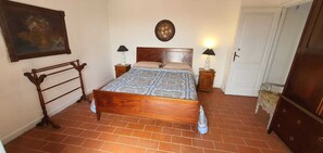 A bedroom with a wooden bed, two bedside tables with lamps, a chair, a dresser, a door, and a wall-mounted painting.