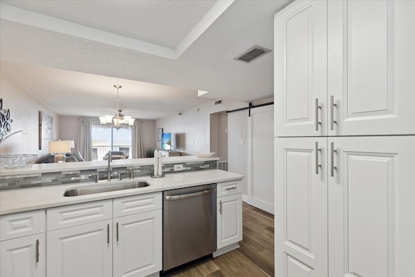 A modern kitchen with white cabinetry, a stainless steel dishwasher, and a large island with a sink. - Top Floor Coastal Paradise | Direct Oceanfront Views, Pool & Private Balcony ☀️ (Cocoa Beach)