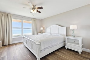 Ein Schlafzimmer mit Bett, Nachttischen, Deckenventilator und Meerblick.