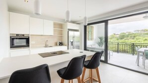 A modern kitchen with a large island, black bar stools, and a view of a balcony with outdoor furniture. - The Breeze at Blue Bay Beach & Golf Resort (Sint Michiel)