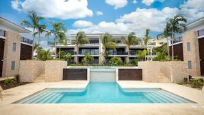 A hotel with a swimming pool, palm trees, and a clear blue sky.